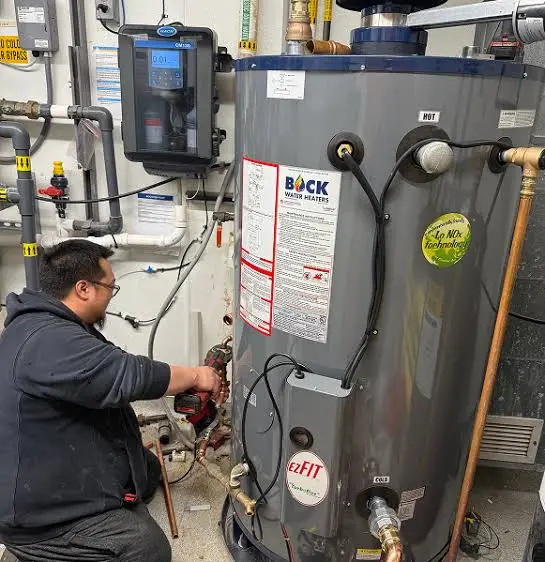 Technician servicing water connections on a commercial-grade water heater with a water-treatment control panel nearby