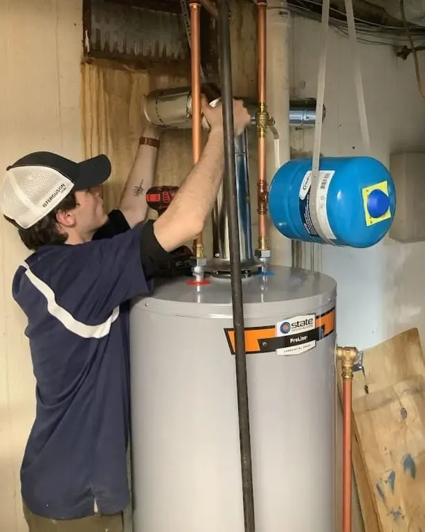 Technician connecting copper water lines and an expansion tank during a water heater service call