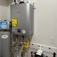Wall-mounted tankless water heater with its water connections and a wall controller alongside