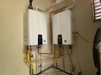 Two wall-mounted tankless water heaters side by side with their gas supply piping